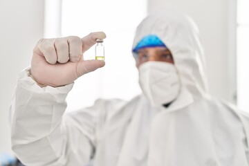 Young latin man scientist wearing covid protection uniform holding vaccine dose at laboratory