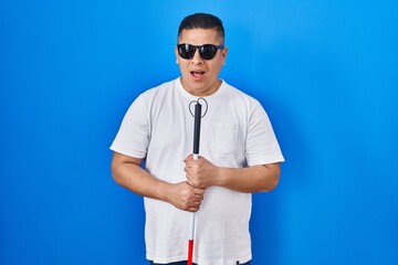 Hispanic young blind man holding cane clueless and confused expression. doubt concept.