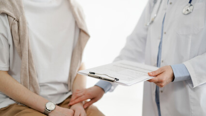 Doctor and patient in clinic. Friendly physician examining a young woman with a one hand while keeping a clipboard with medical records in another. Medicine concept