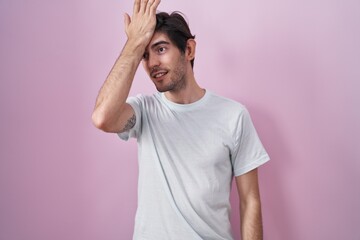 Young hispanic man standing over pink background surprised with hand on head for mistake, remember error. forgot, bad memory concept.