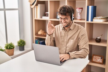 Hispanic young man wearing call center agent headset doing ok sign with fingers, smiling friendly gesturing excellent symbol