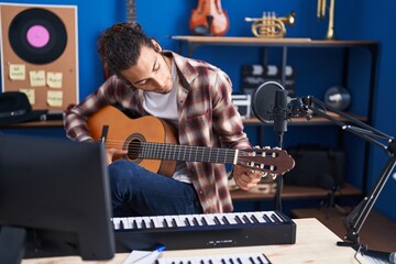 Young hispanic man musician playing classical guitar at music studio