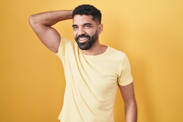 Fototapeta na wymiar Hispanic man with beard standing over yellow background smiling confident touching hair with hand up gesture, posing attractive and fashionable