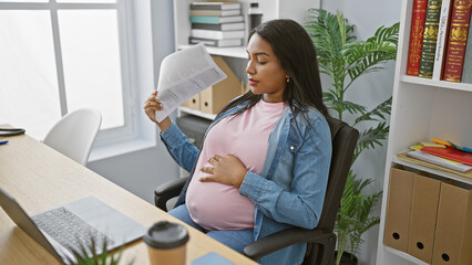 Young pregnant business woman, battling discomfort from the hot office, resorting to using documents as a handfan while immersed in demanding work.