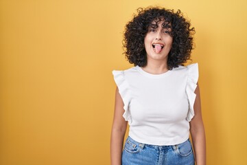 Young middle east woman standing over yellow background sticking tongue out happy with funny expression. emotion concept.