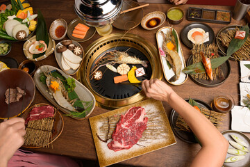 A set of grill food on a wooden table in restaurant.Fresh meat and shrim sliced for grilled menu.Party of friends or family eating dinner on wooden table background.