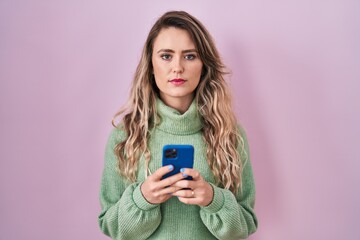 Young caucasian woman using smartphone typing message relaxed with serious expression on face. simple and natural looking at the camera.