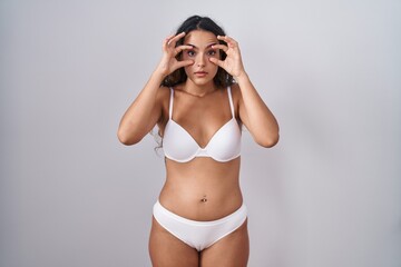 Young hispanic woman wearing white lingerie trying to open eyes with fingers, sleepy and tired for morning fatigue