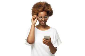 African american woman standing, looking at screen of phone, surfing web and smiling while browsing content