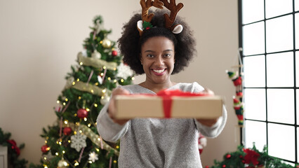 African american woman wearing reindeer ears holding christmas gift at home
