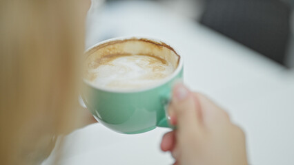 Young blonde woman drinking cup of coffee sitting on table at coffee shop terrace