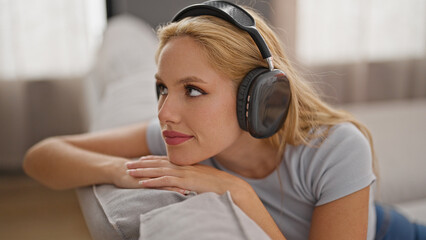 Naklejka premium Young blonde woman listening to music relaxed on sofa at home