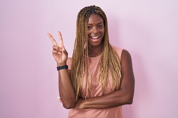 African american woman with braided hair standing over pink background smiling with happy face...