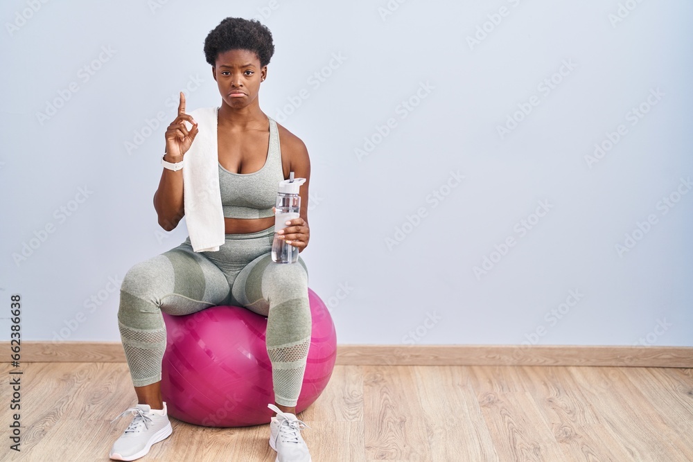 Canvas Prints African american woman wearing sportswear sitting on pilates ball pointing up looking sad and upset, indicating direction with fingers, unhappy and depressed.