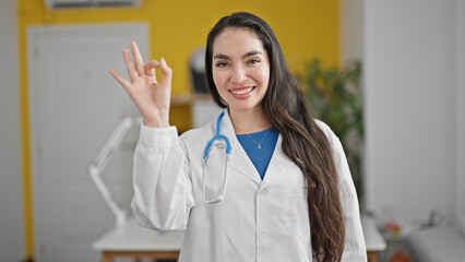 Young beautiful hispanic woman doctor doing ok gesture at the clinic