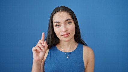 Fototapeta premium Young beautiful hispanic woman smiling confident standing with finger up over isolated blue background