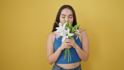 Young beautiful hispanic woman smelling bouquet of flowers over isolated yellow background