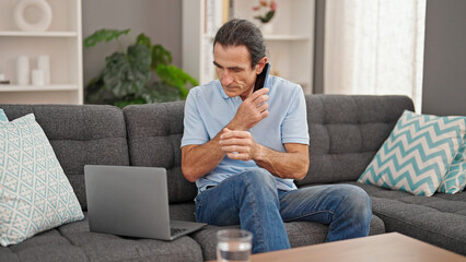 Middle age man talking on smartphone using laptop at home