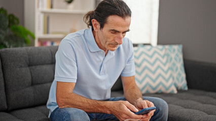 Middle age man using smartphone sitting on sofa at home