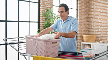 Middle age man holding clothes of basket at laundry room