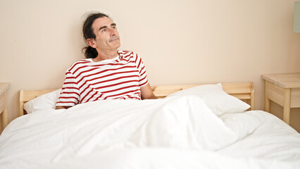 Middle age man sitting on bed with serious expression at bedroom