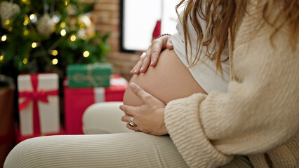 Young pregnant woman massaging belly celebrating christmas at home - obrazy, fototapety, plakaty