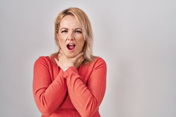 Blonde woman standing over isolated background shouting suffocate because painful strangle. health problem. asphyxiate and suicide concept. - obrazy, fototapety, plakaty