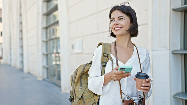 Young beautiful hispanic woman tourist talking on smartphone drinking coffee at street