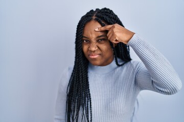 African american woman standing over blue background pointing unhappy to pimple on forehead, ugly...
