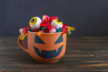 Fototapeta premium Jelly worms and eyes in Halloween cup over dark wooden background.