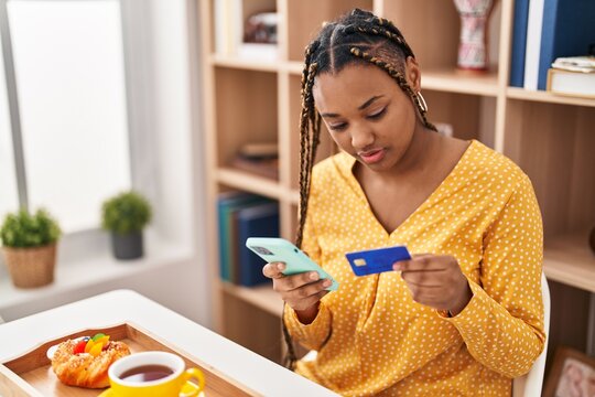 African american woman using smartphone and credit card having breakfast at home