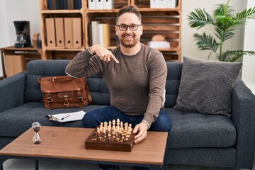 Middle age caucasian man playing chess sitting on the sofa pointing finger to one self smiling...