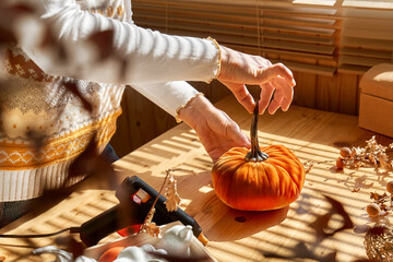Fototapeta na wymiar Woman making orange velvet fabric pumpkin. Autumn decoration with handmade textile pumpkin on wooden table. Fall vibes. Thanksgiving decor.