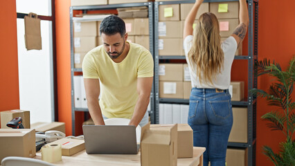 Man and woman ecommerce business workers using laptop holding package of shelving at office