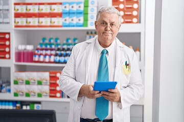 Middle age grey-haired man pharmacist using touchpad working at pharmacy