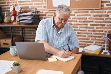 Middle age grey-haired man business worker using laptop writing on notebook at office - obrazy, fototapety, plakaty