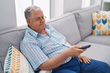 Middle age grey-haired man watching television sitting on sofa at home