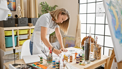 Attractive young blonde woman artist, focused face busy drawing in notebook, indoor art studio - obrazy, fototapety, plakaty