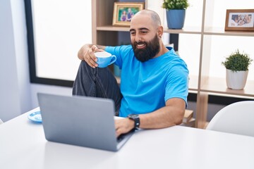 Young bald man using laptop drinking coffee at home