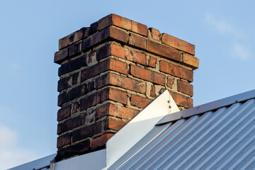  Closeup shot of old, weathered brick chimney against a clear sky.