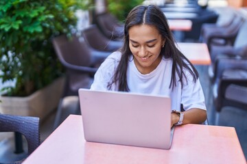 Young beautiful hispanic woman using laptop sitting on table at coffee shop terrace