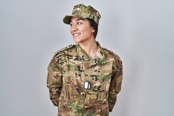 Young south asian woman wearing camouflage army uniform looking away to side with smile on face,...