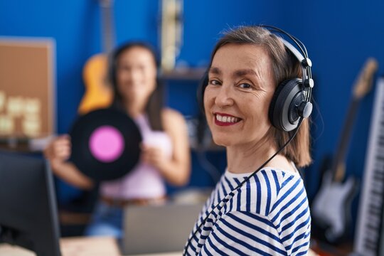 Two women musicians listening to music holding vinyl disc at music studio