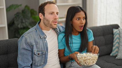 Beautiful couple watching tv eating popcorn surprised at home