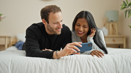 Beautiful couple lying on bed watching video on smartphone at bedroom