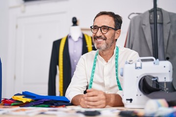 Middle age man tailor smiling confident sitting on table at tailor shop