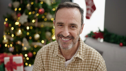 Middle age man smiling confident sitting by christmas tree at home