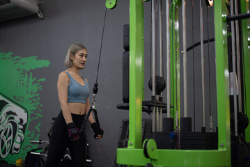 Fototapeta na wymiar Strong young Asian woman exercising with triceps rope pulldown in a fitness club, doing exercises in gym