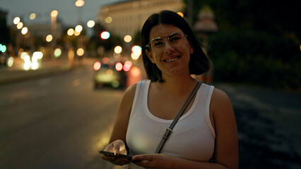 Young beautiful hispanic woman smiling happy using smartphone in the streets at night