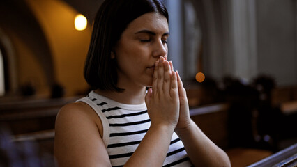 Young beautiful hispanic woman praying on a church bench at Augustinian Church in Vienna